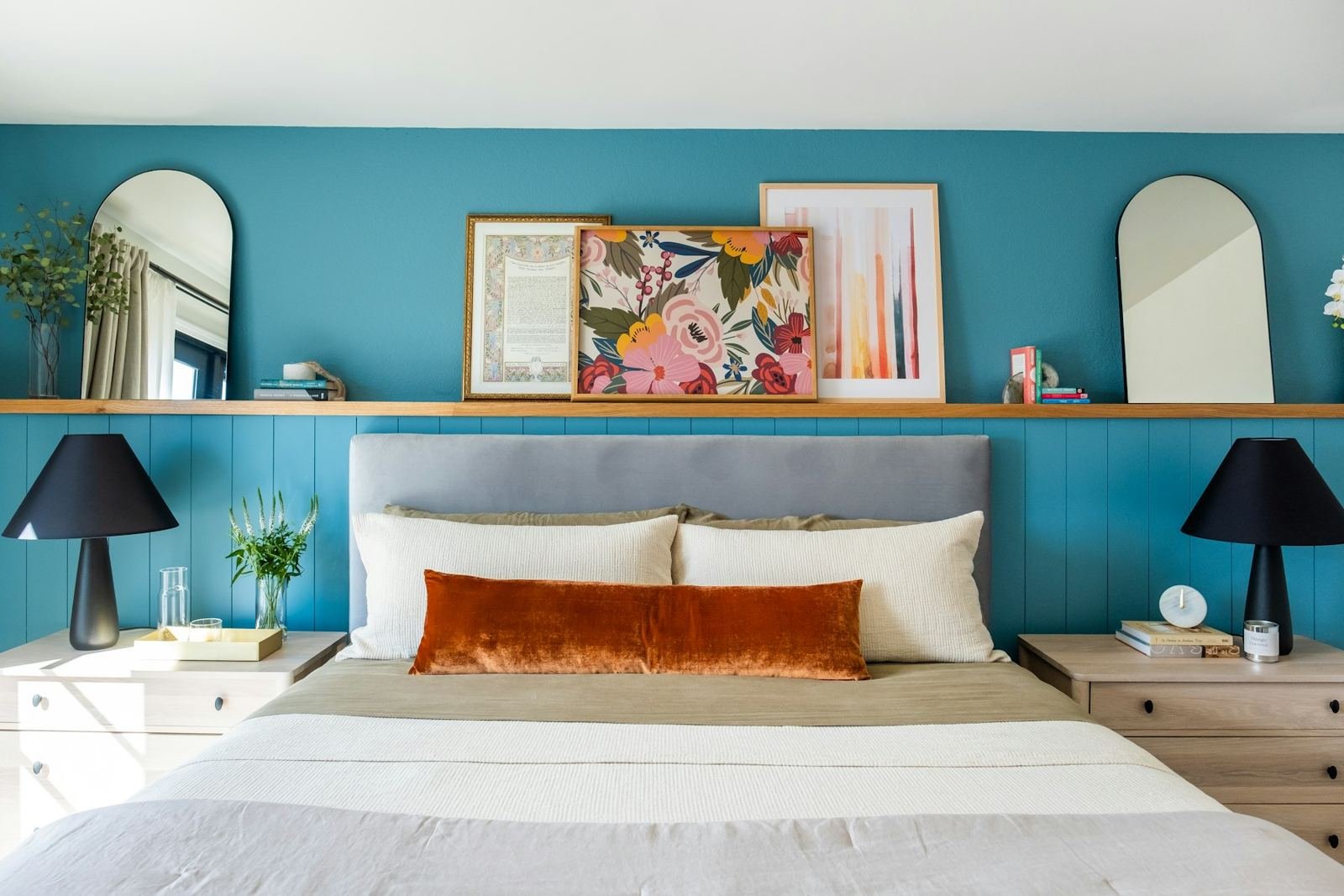 A bedroom with a teal accent wall and orange pillow